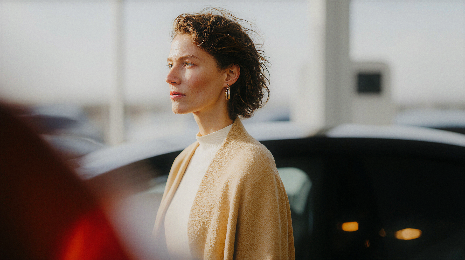 Woman in beige coat beside a car in bright daylight