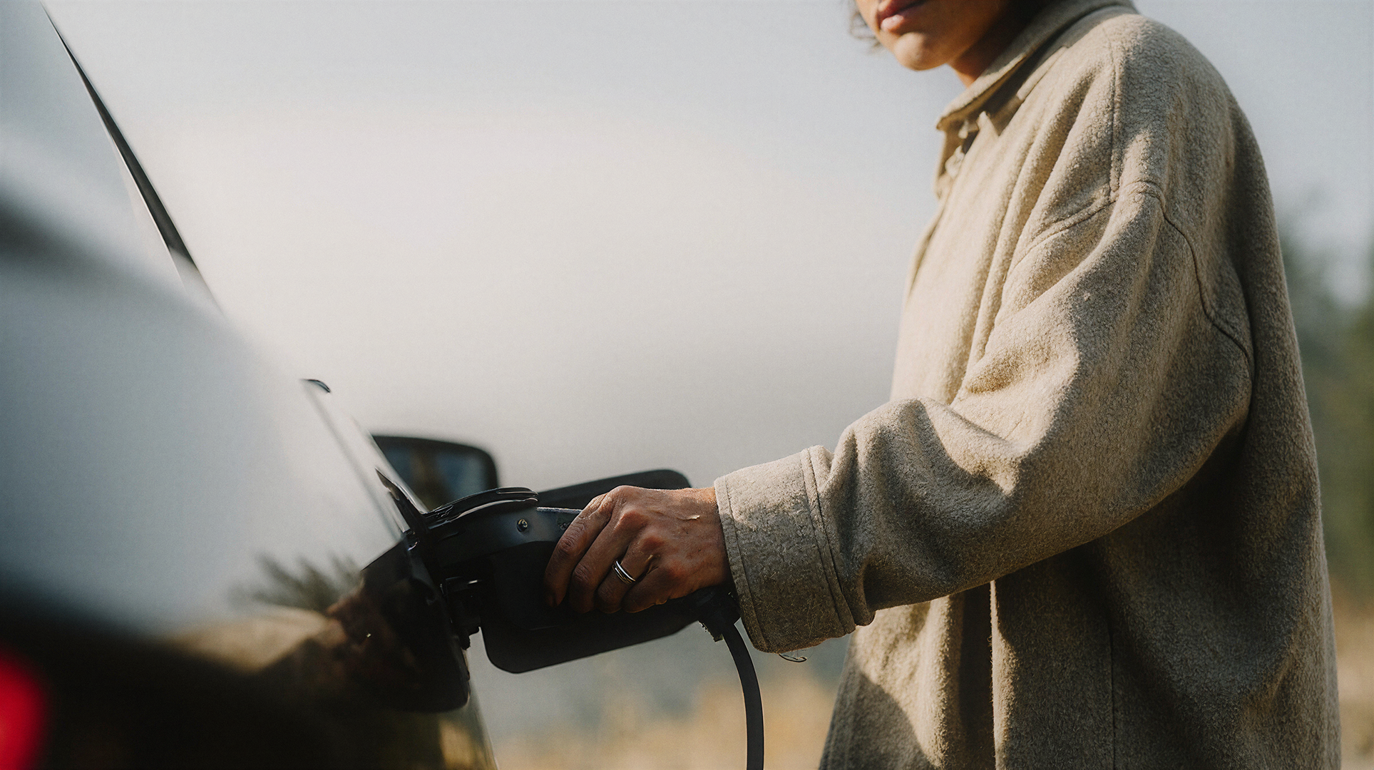 Hand plugging in an EV charger, golden hour